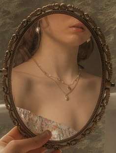 a woman's reflection in a mirror with pearls on her neck and hand holding it