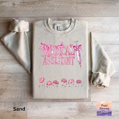 a sweater with the words medical assistant on it and pink flowers in front of it