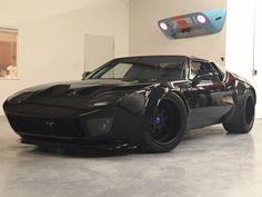 a black sports car is parked in a room with white walls and flooring, while a blue light shines on the ceiling