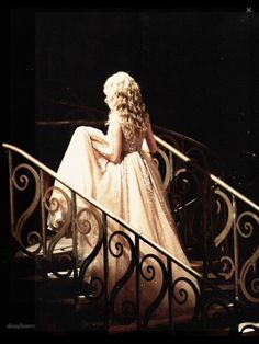 a woman in a white dress is sitting on a stair case and looking down at the ground