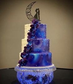 a blue wedding cake with purple flowers and a bride and groom on the top tier