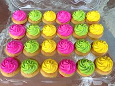 there are many cupcakes with different colors in the tray on the table,