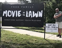 a man standing in front of a movie on the lawn sign with his arms crossed