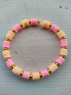 a pink and gold beaded bracelet on a gray surface with yellow beads in the middle