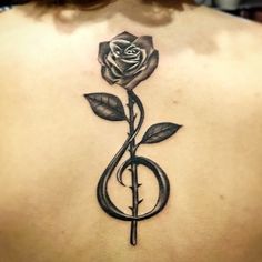 the back of a woman's neck with a rose and treble tattoo on it