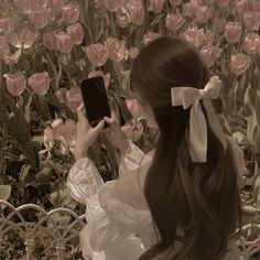 a woman taking a photo with her cell phone in front of pink tulips