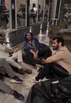 three men sitting on bean bags talking to each other in front of a store window