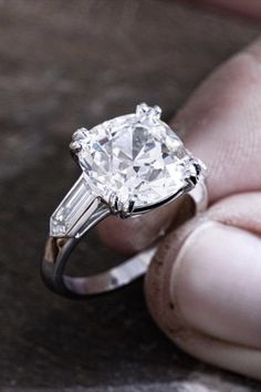 a person holding a ring with a diamond in it's middle and two baguets on the side