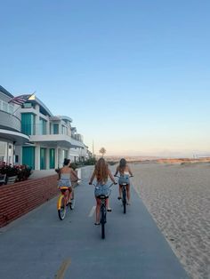 three people riding bikes down a sidewalk next to some houses on the other side of the beach