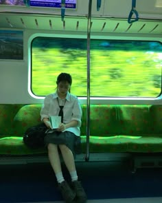 a person sitting on a train seat with a book in their hand and looking out the window