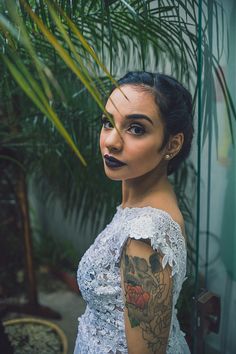 a woman with tattoos on her arms and shoulder posing for a photo in front of a palm tree