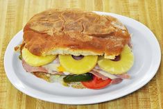 a sandwich with ham, pineapples and tomatoes on a white plate sitting on a wooden table