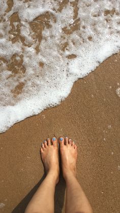 a person standing on the beach with their feet in the sand and water behind them