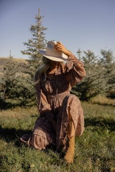 a woman in a dress and hat sitting on the ground with her hands behind her head