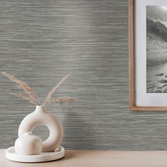 a white vase sitting on top of a wooden table next to a wallpapered wall