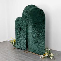 two large green sculptures sitting on top of a wooden floor next to flowers and vases