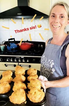 a woman in an apron holding a tray of muffins