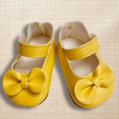 a pair of yellow baby shoes with a bow on the front and bottom, sitting on a beige background