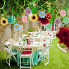 an outdoor table set up for a party with flowers hanging from the ceiling and decorations