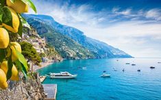 boats are floating on the blue water in front of mountains and houses with yellow fruit hanging from them