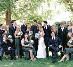 a large group of people in formal wear posing for a photo on the grass with trees behind them