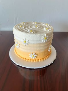 a white cake with yellow and white frosting on a wooden table next to a wall