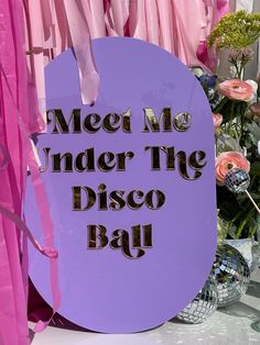 there is a sign that says meet me under the disco ball on display in front of pink curtains