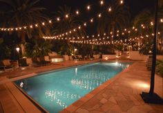 an outdoor swimming pool with lights strung over it