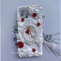 a white case with red roses on it and a gold rose in the middle is surrounded by flowers