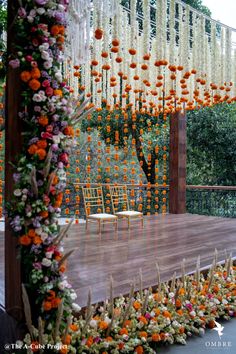 an outdoor stage decorated with orange and white flowers, chairs and greenery on the side