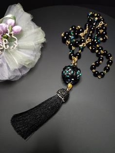 Beautiful sautoir necklace with long tassel. The main elements of this necklace are two: a large 30 mm pearl covered in beads and crystals and a splendid black tassel with Marcasite. These crystals give a lot of brightness and make the necklace very elegant. The pearl is covered by hand with different types of beads, a precision and difficult job to perform. The necklace is made with black agate beads of different sizes and crystals. Some points are highlighted with the beautiful emerald green color which gives a mystical look to the necklace. Everything matches perfectly, colors and shapes. The closure is an 18K gold-plated opening ring. The pendant with the ball and the tassel can be removed if desired and you can only wear the simple necklace. The necklace is very elegant, perfect for l Elegant Necklace With 108 Beads For Gift, Elegant Necklace With 108 Beads Pendant, Elegant Black Long Necklace For Gift, Elegant Necklace With 108 Beads For Party, Elegant Party Necklace With 108 Beads, Elegant Black Tassel Necklace For Party, Tassel Necklace With Round Beads For Gifts, Elegant Jewelry With Tassels And Round Beads, Elegant Tassel Necklace With Round Beads