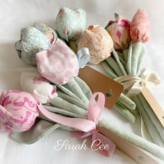 several different types of fabric flowers on a white table cloth with tags attached to them