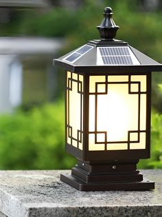 a lamp that is sitting on top of a stone block in front of some bushes