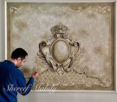 a man is working on an ornate wall decoration in front of a large framed painting