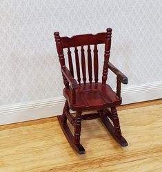 a wooden rocking chair sitting on top of a hard wood floor next to a wall