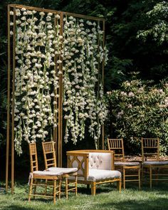 an outdoor seating area with white flowers on the wall and wooden chairs in the grass