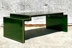 a green table sitting on top of a cement ground next to a white brick wall