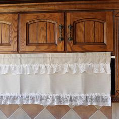 a kitchen with wooden cabinets and white lace on the valance above the cabinet doors