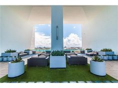 an outdoor lounge area with couches and potted plants on the grass in front of it