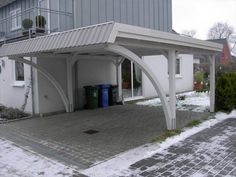 a white building with a metal roof in the middle of it's driveway and snow on the ground