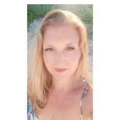 a woman with blonde hair and blue eyes posing for a photo on the beach in front of some grass