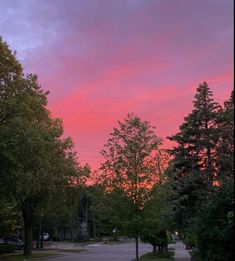 the sky is pink and purple as the sun goes down in the distance behind some trees