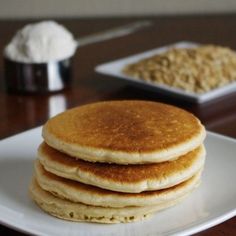 three pancakes are stacked on a white plate next to a bowl of oatmeal