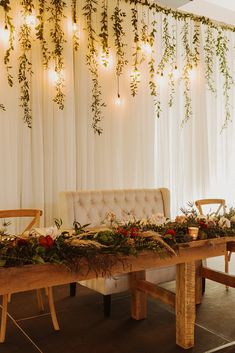 a table with flowers and greenery on it in front of a white drapes