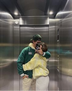 a man and woman standing in front of an elevator taking a photo with their cell phone