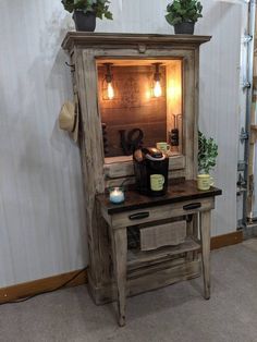 an old wooden cabinet with potted plants on top and a lighted mirror above it