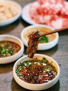 chopsticks holding up food in small bowls with dipping sauces on the side