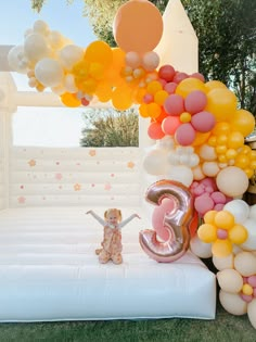 an inflatable balloon arch with balloons and a teddy bear on the ground next to it