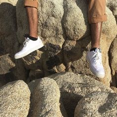 a man standing on top of a large rock covered in lots of white shoes and tan pants