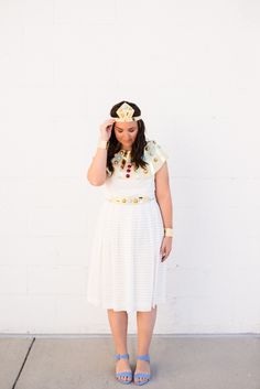 a woman in a white dress is standing against a wall and has her hands on her head